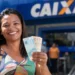 Mulher sorri segurando notas de real em frente a uma agência da Caixa, ilustrando saque de R$ 3.950 do FGTS até 30 de junho