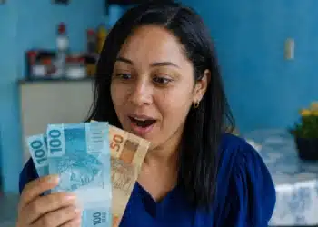 Mulher segurando notas de dinheiro, representando o saque do FGTS de até R$ 6.220 para moradores da BA, RJ e MG.