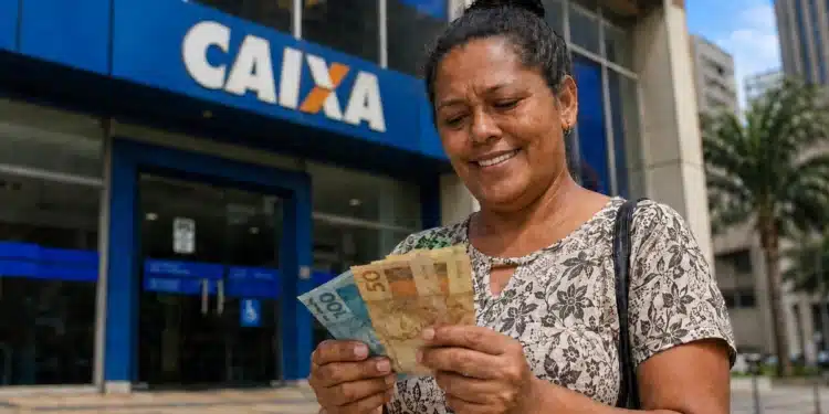 Mulher sorrindo ao segurar cédulas de real em frente a uma agência da Caixa, representando a solicitação do saque de R$ 6.220.
