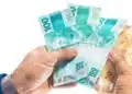 Mãos segurando notas de reais ilustrando o benefício de R$ 6.220, que pode ser solicitado até segunda-feira, 29 de junho.