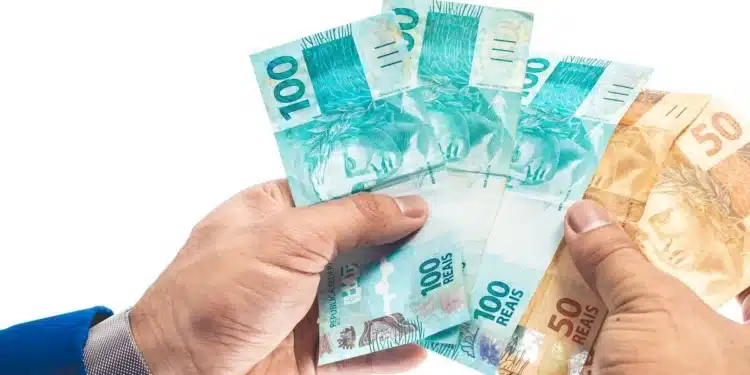 Mãos segurando notas de reais ilustrando o benefício de R$ 6.220, que pode ser solicitado até segunda-feira, 29 de junho.