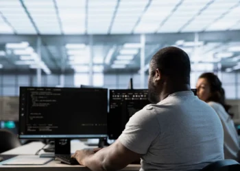 Profissional de tecnologia trabalhando em computadores em escritório moderno, representando carreira em TI em 2026.