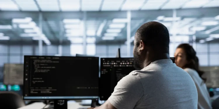 Profissional de tecnologia trabalhando em computadores em escritório moderno, representando carreira em TI em 2026.
