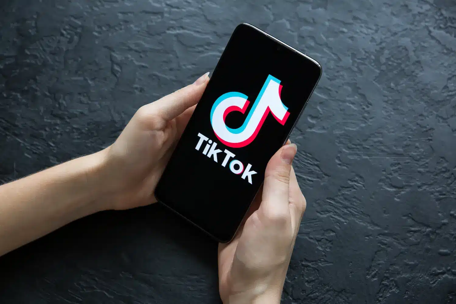 Guia para criar e remover Destaques no TikTok Pessoa segurando celular com logo do TikTok na tela para ilustrar guia sobre Stories fixados no perfil.