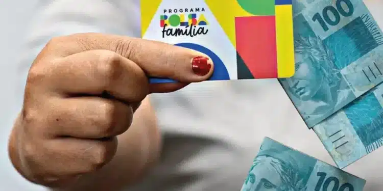 Mão segurando cartão do Bolsa Família com cédulas de real ao lado, representando os últimos pagamentos de junho do programa social.