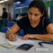 Mulher de camiseta azul marinho preenche formulário com caneta em balcão, ao lado de passaporte brasileiro e RG.
