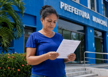 Mulher lê documento de concurso público em frente à Prefeitura Municipal.