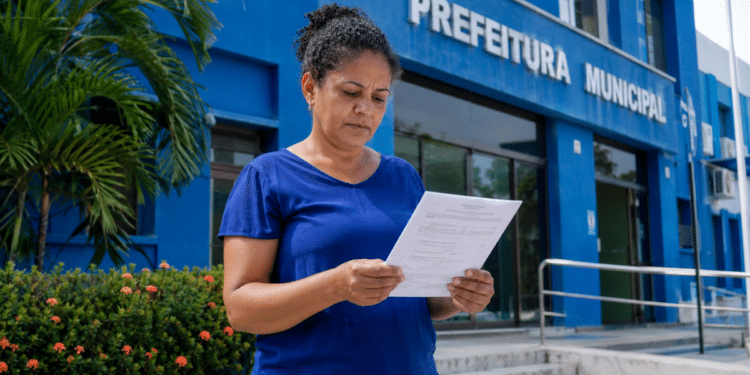 Mulher lê documento de concurso público em frente à Prefeitura Municipal.