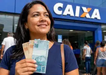 Mulher segura cédulas de real em frente a uma agência da Caixa, representando a liberação ou solicitação do valor de R$ 2.900.