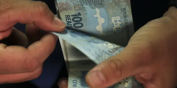 Pessoa conta cédulas de cem reais com as duas mãos