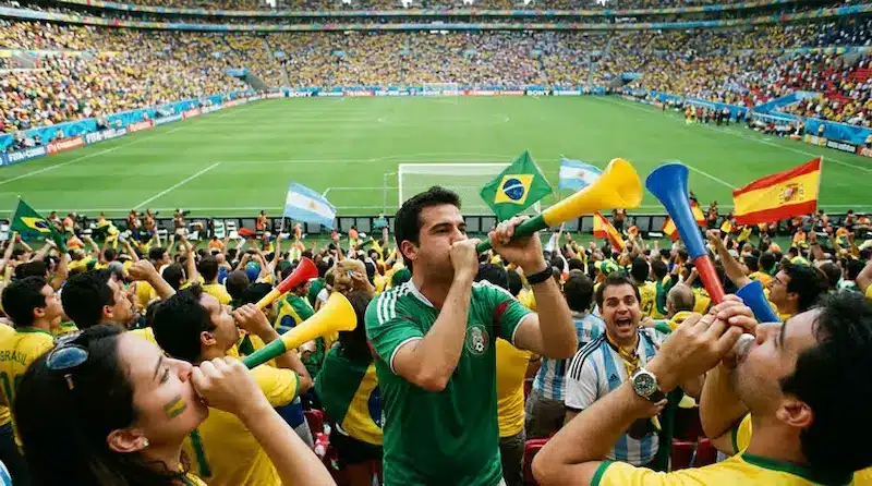 Torcida em estádio usando vuvuzelas, ilustrando restrições de segurança da FIFA.