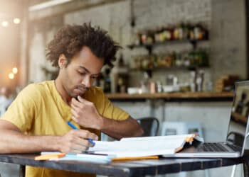Candidato de camiseta amarela estudando com caderno e apostila após o resultado final da 2ª edição do CNU