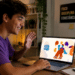 Jovem sorridente de camiseta roxa acena para notebook exibindo logo Rede Pode Falar, em mesa com livros.