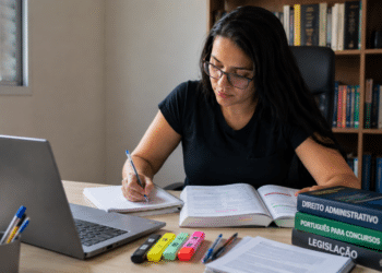 Jovem mulher estudando em mesa com livros jurídicos, laptop e bandeira do Brasil.