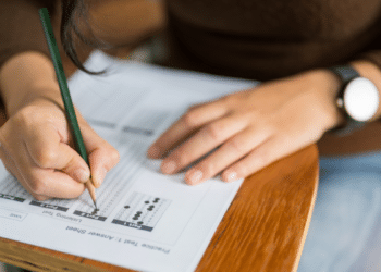 Jovem responde prova de múltipla escolha simulada em mesa escolar.