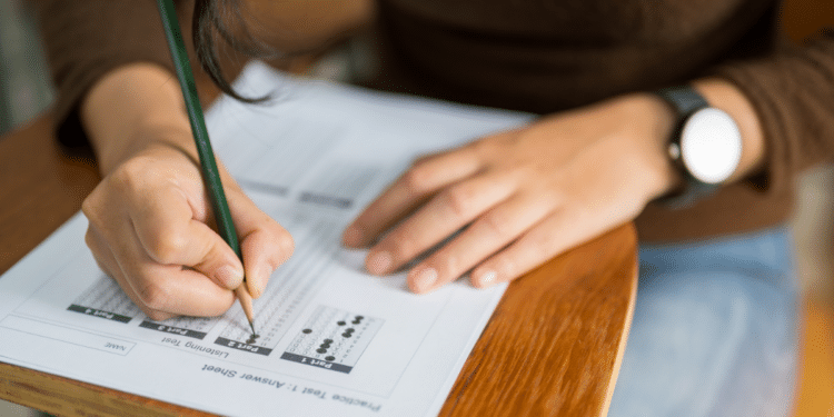 Jovem responde prova de múltipla escolha simulada em mesa escolar.