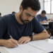 Homens e mulheres adultos respondendo teste de múltipla escolha em sala iluminada, com foco em homem preenchendo folha.