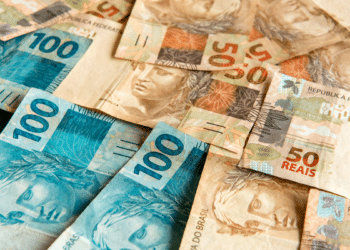 Notas de 50 e 100 reais espalhadas sobre superfície.