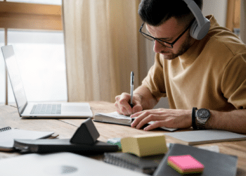 Jovem concentrado estudando com fones de ouvido e notebook em ambiente doméstico.