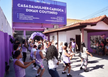 Mulheres vestidas de blusas roxas reunidas em ambiente externo.