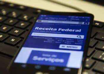 Tela de celular exibindo site da Receita Federal sobre teclado preto de computador