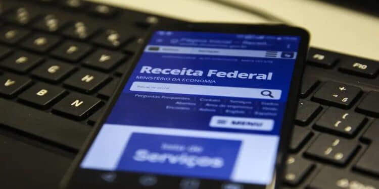 Tela de celular exibindo site da Receita Federal sobre teclado preto de computador