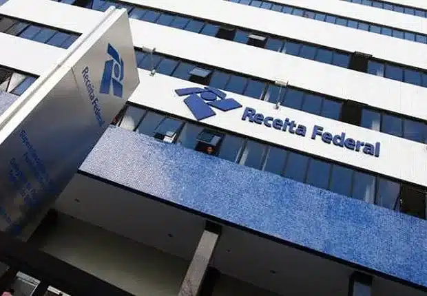 Receita Federal centraliza atendimento digital e encerra serviço Fale Conosco Fachada de prédio da Receita Federal com logo azul e letras na entrada, vista em ângulo