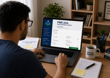 Homem preenche inscrição da PND 2026 no notebook, com materiais de estudo e caneca com mensagem sobre educação.