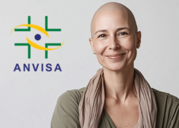Mulher adulta careca sorri ao lado do logo da ANVISA em fundo claro.