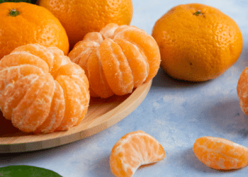 Tangerinas frescas inteiras e descascadas em fundo azul claro.