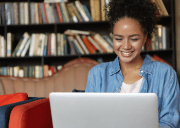 Jovem sorrindo trabalhando em laptop em biblioteca moderna.