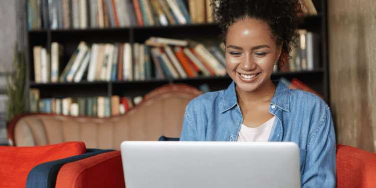 Jovem sorrindo trabalhando em laptop em biblioteca moderna.