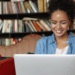 Jovem sorrindo trabalhando em laptop em biblioteca moderna.