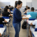Fiscal de concursos entrega provas em sala com estudantes em exame.