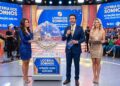 Três apresentadores em estúdio exibindo sorteio da Loteria dos Sonhos, com globo, bolas e plateia