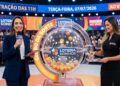 Apresentadoras da Loteria dos Sonhos no sorteio das 11h com globo da sorte e plateia ao fundo
