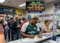 Homens e mulheres em fila na lotérica, homem com camisa do Palmeiras faz aposta na Mega-Sena 3028