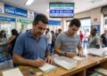 Dois homens preenchem bilhetes da Mega-Sena em casa lotérica com aviso de prêmio de R$ 20 milhões ao fundo