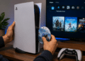 Mãos masculinas inserem disco God of War Ragnarok em um PlayStation 5 branco, com controle DualSense próximo, planta decorativa, menu do console exibindo jogos como Horizon, Spider-Man e God of War.