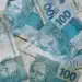 Notas de R$ 100 do real brasileiro sobrepostas, ilustrando a liberação do abono salarial PIS/Pasep no mês de julho.