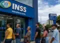 Fila de segurados em frente a uma agência do INSS, com fachada azul em destaque, relacionada a projeto sobre aposentadoria maior.