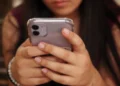Usuária segurando smartphone em destaque, representando atualizações de segurança da Apple contra ameaças digitais impulsionadas por inteligência artificial.
