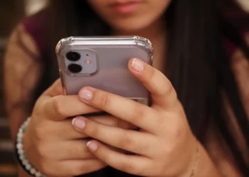 Usuária segurando smartphone em destaque, representando atualizações de segurança da Apple contra ameaças digitais impulsionadas por inteligência artificial.