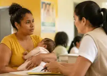Mãe brasileira segura recém-nascido durante atendimento social, representando as ações necessárias para atualizar o Bolsa Família após o nascimento de um membro ou mudanças na família.
