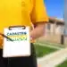 Imagem ilustrativa de atendente de colete amarelo segurando prancheta com a marca do Cadastro Único diante de casas de conjunto habitacional.