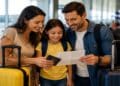 Família com criança, malas e passaporte no aeroporto, ilustrando a autorização de viagem para menores nas férias escolares.
