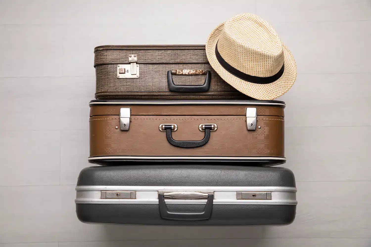 Bagagem Três malas de viagem empilhadas com um chapéu, representando o significado literal da palavra bagagem.