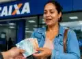 Mulher recebendo notas de reais em frente a uma agência da CAIXA, representando pagamentos de benefícios liberados em julho