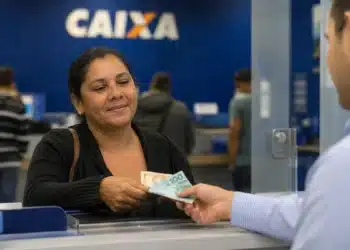 Beneficiária recebendo dinheiro em uma unidade da Caixa Econômica Federal, representando o pagamento antecipado do Bolsa Família de julho em 175 municípios.