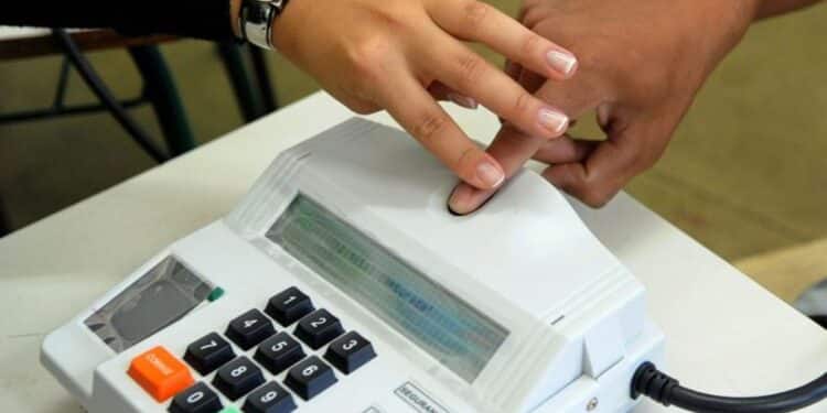 Imagem ilustrativa de eleitor pressionando o dedo no leitor biométrico acoplado ao terminal usado pelo mesário, equipamento com teclado numérico e botões de correção e confirmação
